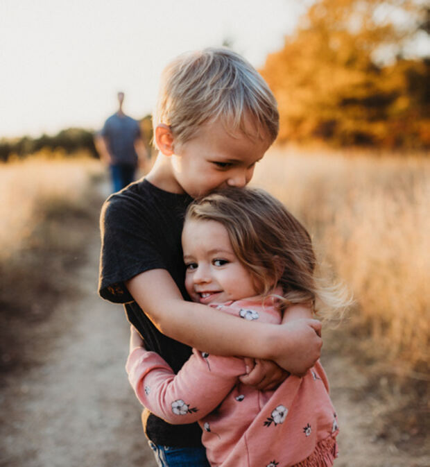 Two young siblings hugging in a field of dry grass